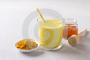 Golden milk with turmeric in a glass with honey on a gray stone