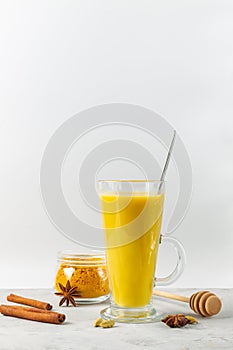 Golden milk with turmeric and honey in a tall glass. Spiced latte, vertical with space.