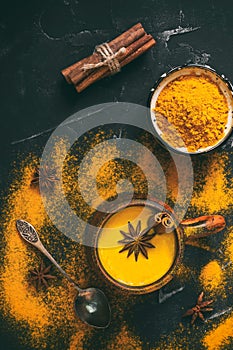 Golden milk with turmeric powder, cinnamon and star anise in a ceramic cup on a black stone background. Natural drink for colds