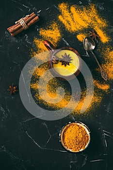 Golden milk with turmeric powder, cinnamon and star anise in a ceramic cup on a black stone background. Natural drink for colds