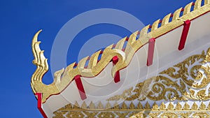 Golden Naga pattern on ornamental Thai temple roof against blue sky background