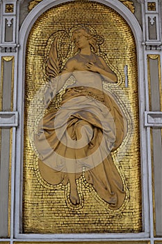 The golden niche, on the wall of a historic building, contains the statue of a woman with a palm branch in her hand.