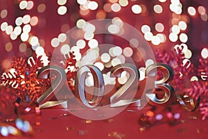 Golden numbers of year 2023. Glowing festive garland with bokeh on red background.