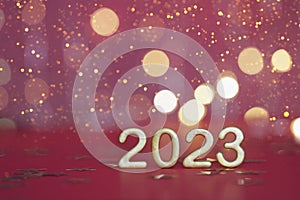 Golden numbers of year 2023. Glowing festive garland with bokeh on red background.