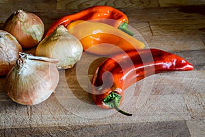 Golden onions and sweet organic pointed peppers on a wooden cutting board close up