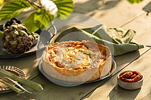 Golden organic healthy crispy pie with artichokes, dried tomatoes and olives on the table