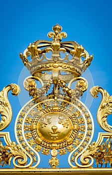 Golden ornate gate crown of Chateau de Versailles on blue sky background. Paris, France,