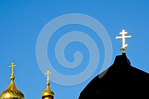 A golden Orthodox cross shines from sun against a blue sky. Christian photo with copy space