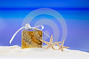 Golden packed gift box with yellow stars at tropical ocean beach. Christmas, New Year, birthday vacation in hot countries