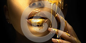 Golden paint smudges drips from the face lips and hand, golden liquid drops on beautiful model girl`s mouth, creative makeup