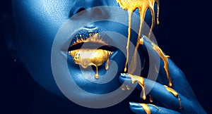 Golden paint smudges drips from the face lips and hand, golden liquid drops on beautiful model girl`s mouth, creative makeup