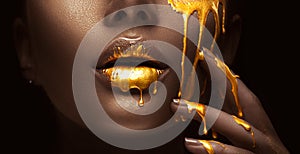 Golden paint smudges drips from the face lips and hand, golden liquid drops on beautiful model girl`s mouth, creative makeup