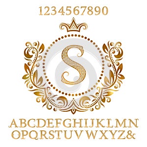 Golden patterned letters and numbers with initial monogram in coat of arms form. Shining font and elements kit for logo design