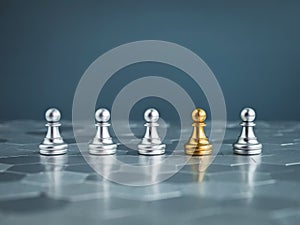 The golden pawn chess piece standing in the group of silver pawn chess pieces on hexagon pattern floor.