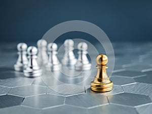 The golden pawn chess piece standing out from the group of silver pawn chess pieces on hexagon pattern floor.