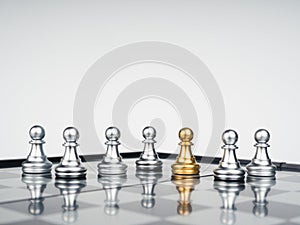 The golden pawn chess piece standing out of the group of silver pawn chess pieces on chessboard.