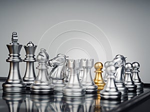 The golden pawn chess piece standing stand in the middle many silver chess pieces.