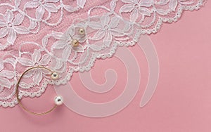 Golden with pearl bracelet and golden earrings on floral white textile on pink background with copy space