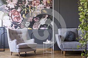 Golden pendant light above a cozy armchair in a fancy living room interior with molding and floral print on gray walls