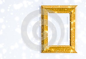 Golden photo frame and glowing glitter snow on marble flatlay background for Christmas and winter holidays