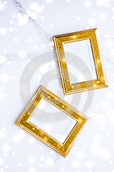 Golden photo frame and glowing glitter snow on marble flatlay background for Christmas and winter holidays