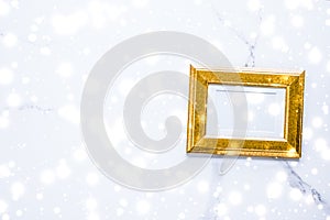 Golden photo frame and glowing glitter snow on marble flatlay background for Christmas and winter holidays