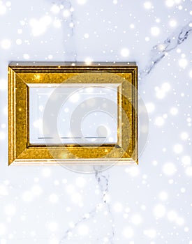 Golden photo frame and glowing glitter snow on marble flatlay background for Christmas and winter holidays