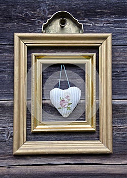 Golden picture frame on wooden wall and cloth heart