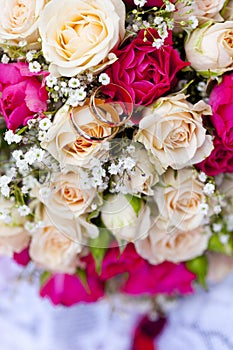 Golden wedding rings on wedding bouquet of pale pink and crimson or red roses