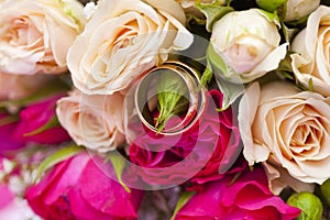 Golden wedding rings on wedding bouquet of pale pink and crimson or red roses