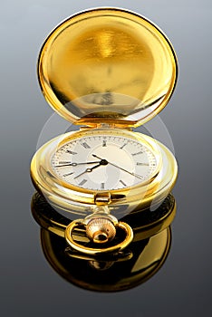 Golden pocket watch on glass with reflection