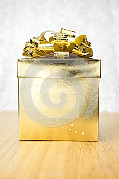 Golden present box with big bow on wooden table at bokeh white b
