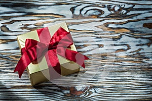 Golden present box with red knot on wooden board