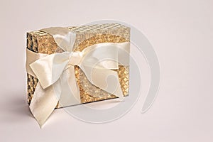 Golden present box with a silk bow on pastel background. Copy space.