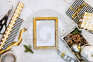 Golden ptoto frame, gift boxes, a crate full of pine cones and christmas toys and wrapping materials on a white wood old backgroun