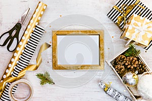 Golden ptoto frame, gift boxes, a crate full of pine cones and christmas toys and wrapping materials on a white wood old backgroun