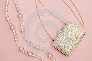 Golden purse and pearl necklace on pink background