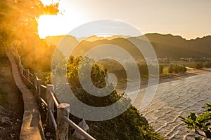 Golden rays of sun on the mountain horizon atop an old path along the edge of the ocean with small waves rolling in toward the As