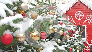 Golden and Red Balls Hanging on the Christmas Tree Covered With Snow and Red Gingerbread House. Beautiful Decorated