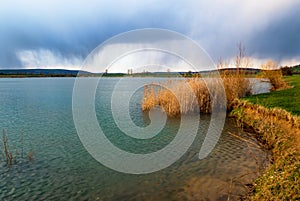 Golden reed on lake shore, dramatic sky with rain water streams on horizon