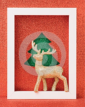 Golden reindeer ornament on a white wooden frame. Christmas red glitter background.