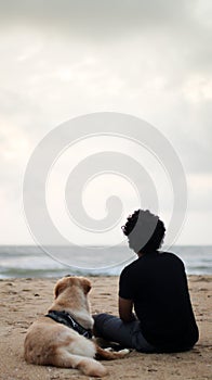 a golden retriever dog and his person sitting together on the beach sand