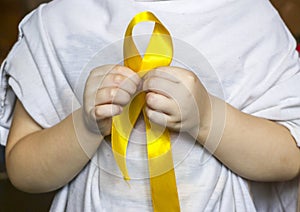 Golden ribbon in the hands of child. Concept: pediatric oncology, children`s cancer