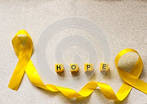 Golden ribbon and words made up of children`s plastic beeches. concept - a symbol of childhood cancer, pediatric oncology