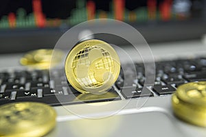 Golden Ripple coin with gold coins lying around on a black keyboard of silver laptop and diagram chart graph on a screen