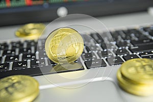 Golden Ripple coin with gold coins lying around on a black keyboard of silver laptop and diagram chart graph on a screen