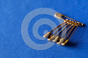 Golden safety pins on blue background, closeup. Space for text