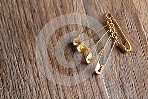 Golden safety pins on wooden table, flat lay. Space for text