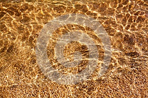 Golden sand under clear sea water and sunlight glow reflection close up top view, yellow sandy texture below ocean water