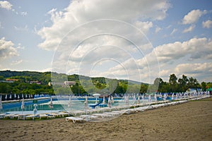 Golden sand and white beach chairs with umbrella around the big swimming pool in Strand Ostroveni from Ramnicu Valcea. Romania -